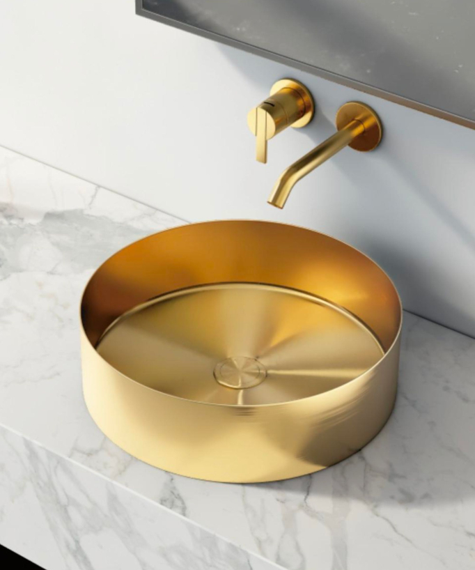 Vasque ronde en acier inoxydable doré brossé, posée sur un plan de travail en marbre et complétée par un mitigeur mural de lavabo doré brossé